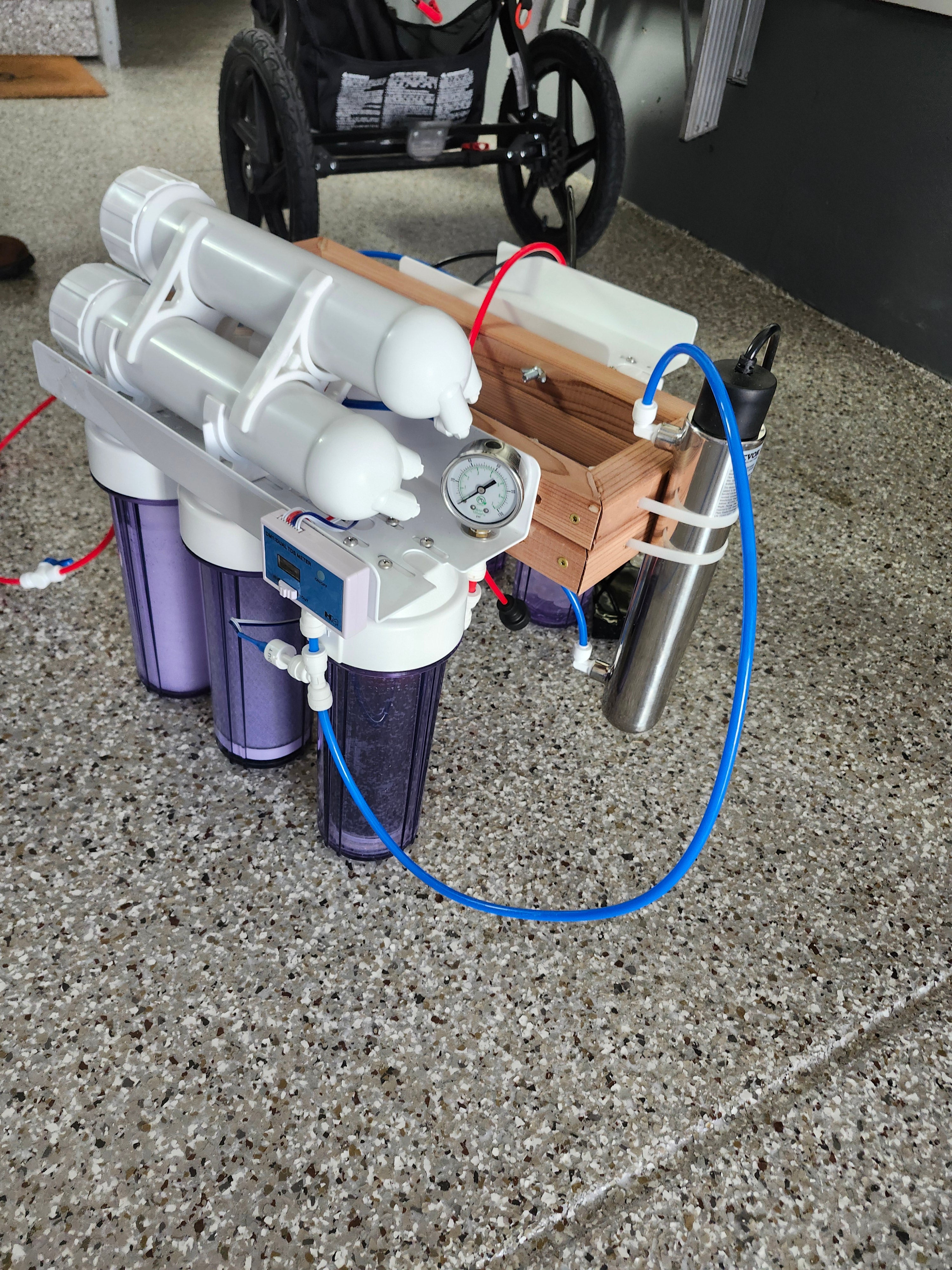 Portable Rius reverse osmosis unit with crystal-filled charging chambers and a pressure gauge on a garage floor